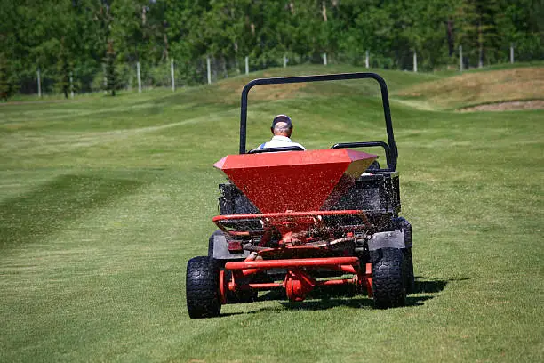 Applying fertiizer on a golf course. Fertilizer spreading machine on a golf course in summer. A maintenance employee at a golf course is applying nitrogen and other nutrients into the soil for enhanced growth. Themes include agronomy, turf, turf management, greens keeper, maintenance employee, fertilizer, growing, cutting, lawn, turf grass maintenance, applications, and fungicide. 