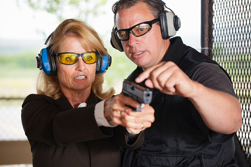 A firearm shooting instructor assisting a student at a shooting range.