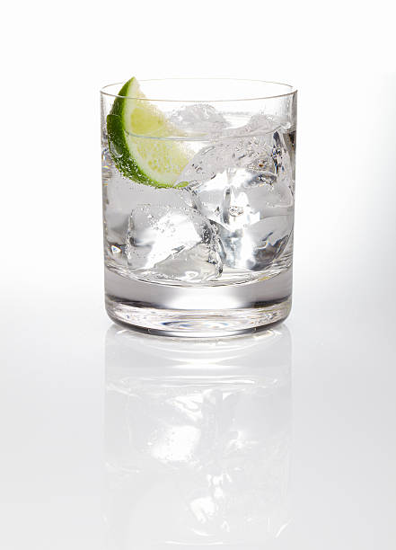 A glass of gin and tonic with ice and a slice of lime  Gin and tonic with wedge of lime shot on reflective white background. vodka stock pictures, royalty-free photos & images