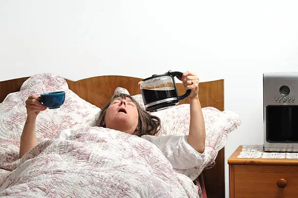 Woman too tired to wake up, holding coffee jug and cup. Could be used to show unhealthy lifestyle, tiredness, stress, sleep problems or bad home-work balance