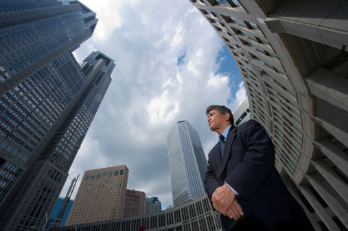 Senior business executive standing confidently with office buildings in the background in Shinjuku, Tokyo.
