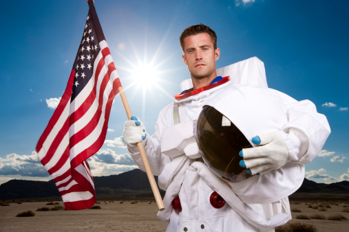 Portrait of an american astronaut holding the US flag and his helmet with the sun in the background.