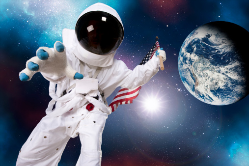 Low angle view of an astronaut on the surface of another moon or planet, holding an american flag and leaning over, reaching for something with a beautiful view of the universe and the planet earth in the background.