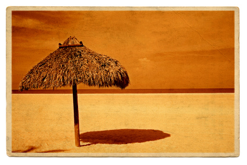 Vintage travel postcard of straw umbrella beach shelter on grunge paper with sepia toning.