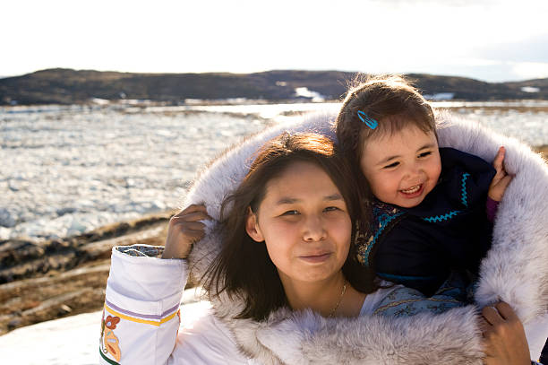 Inuit Mother and Daughter Traditional Dress Baffin Island Nunavut An Inuit mother has her daughter in her amouti, a traditional way to carry the young people.  This is on the tundra of Baffin Island, Nunavut, Canada in late spring. Smiling.  Copy space.  indigenous peoples of the americas stock pictures, royalty-free photos & images