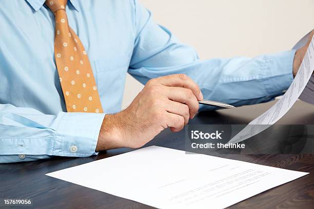 A Businessman Holding Papers At A Desk Stock Photo - Download Image Now - Blue, Brown, Business