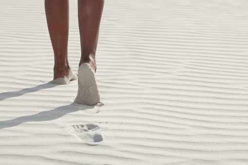 Close up photo of woman's legs walking on a white Australian sand beach.
