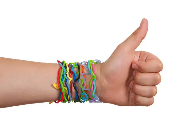 Seen here is a close –up of a nine-year-old’s arm and hand wearing silly shaped rubber band bracelets on the wrist.  Hand is giving thumbs up sign. These are the latest rage in children’s fashion and collecting.  The bands take the shape of animals, dinosaurs, food and countless other shapes.  Children collect trade and then wear the bands.  Bands shown here are made from both silicone and rubber. Release included for hand model.