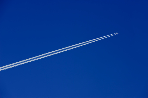 A distant airplane, aeroplane leaving a vapour trail from its four jet engines far up in a deep blue sky