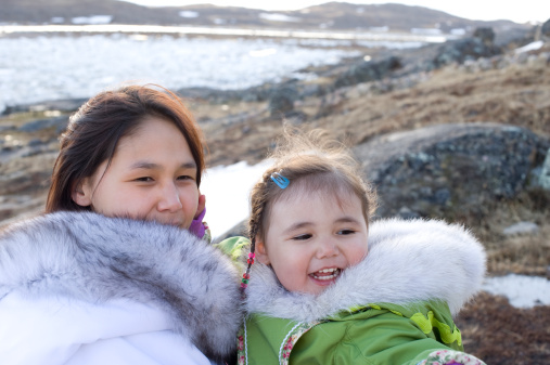 An Inuit mother with her daughter on the barrens of remote Baffin Island, Nunavut Territory, Canada.  They wear traditional agouti parkas.  the background is rock and ice with distant mountains.
