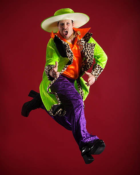 Brightly Dressed Man in Mid-Air A young man wearing brightly colored clothing in a mid-air pose against a red beckground. pimp hat stock pictures, royalty-free photos & images