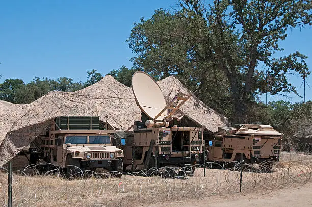 Truck mounted military satellite communications with desert camouflage and barbed wire.