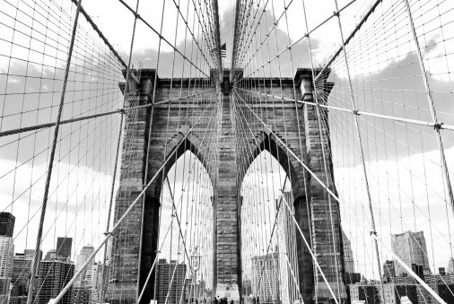 A symmetrical, high contrast, black and white image of the Brooklyn Bridge in New York City spanning the Manhattan and Brooklyn boroughs with the Manhattan skyline in the distance. 