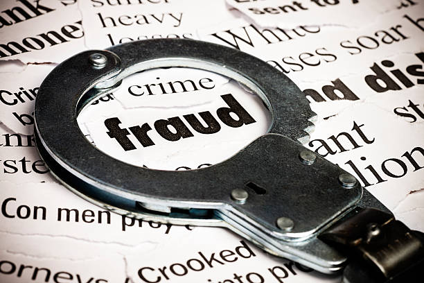 Handcuffs over newspaper with the word fraud stock photo