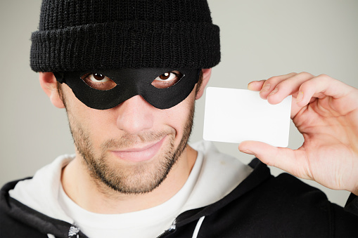 A masked burglar/thief holding blank credit cards.