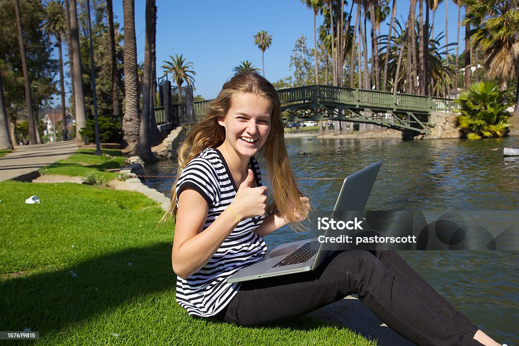 Beautiful Teen Girl on Laptop Smiles with Thumbs Up Young caucasian blonde 14 year old girl holds computer on her lap with a big thumbs up in a southern California park in Los Angeles while smiling on summer day California Stock Photo