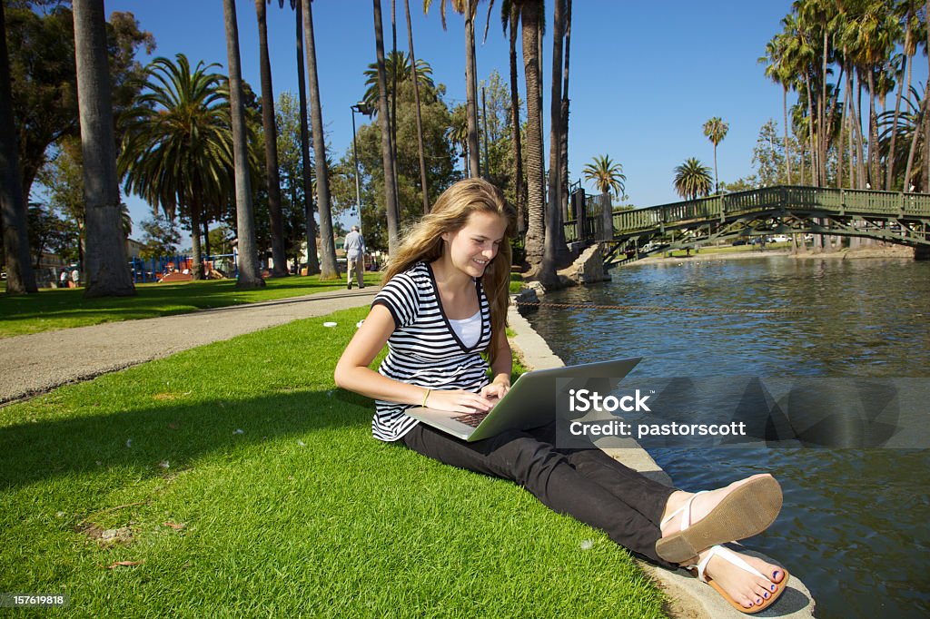 Pretty Teenage Girl Reading on Laptop in Park Los Angeles Young caucasian blonde 14 year old girl holds a laptop on her lap while reading in a southern California park in Los Angeles while smiling on summer day 14-15 Years Stock Photo