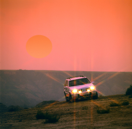 Sport Utility Vehicle driving off-road with large Sun in a red sky at Sunset