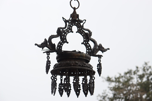 Antique traditional metal diya with clear blue sky background hanged on the temple roof.