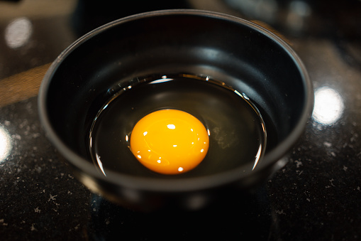 Fresh raw egg in black bowl dish. Close up