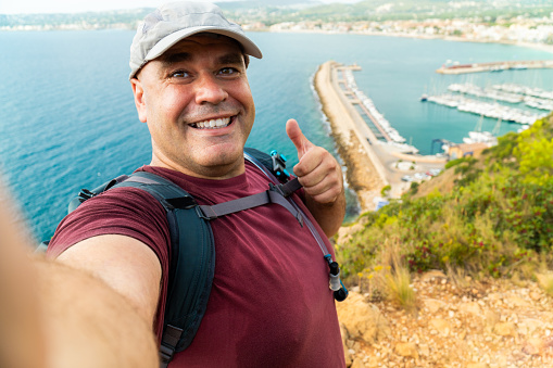Happy hiker takes a selfie outdoors, with the sea on background