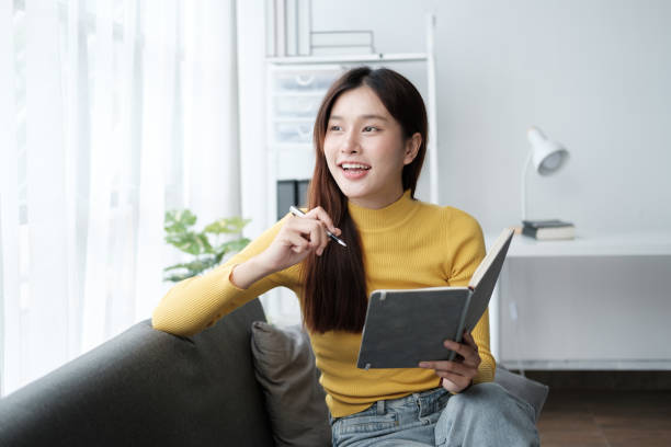 istock Pretty beautiful girl reading a book at sofa, studying and learning while relaxing on the sofa in the living room. 1576285063