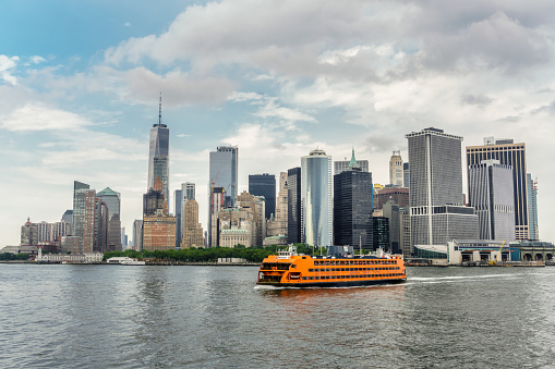 New York, NY, US-July 27, 2018: View of the orange Staten Island Ferry as it approaches lower Manhattan with view of skyline and the Freedom tower.