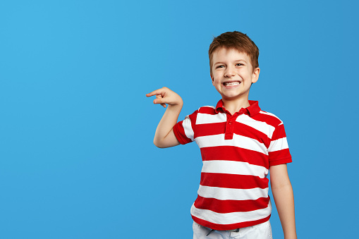 Wow look, advertise here. Portrait of excited cute little kid boy in red striped polo shirt pointing to empty space on background, surprised preschooler showing copy space for promotional ad