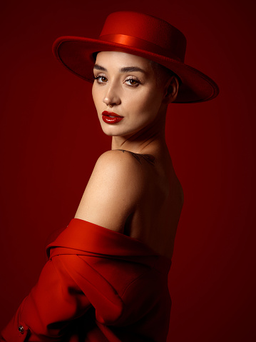 Portrait, fashion and a woman runway model on a red studio background for elegant or trendy style. Aesthetic, art and beauty with a young female person looking over her shoulder in a classy outfit