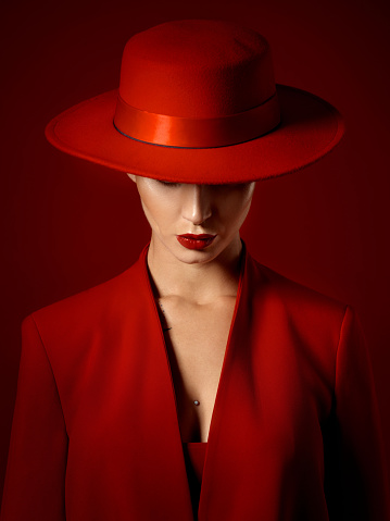 Suit, hat and woman with fashion or beauty in studio with retro, style or edgy, confident or creative pose on red background mockup. Mystery character, model and girl with power or vintage aesthetic