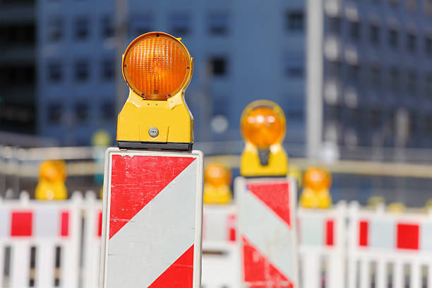 A construction worker carefully positions a safety barrier on a bustling city street, ensuring safety precautions are in place for pedestrians and vehicles during daytime.