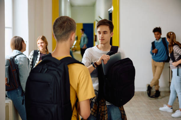 istock High school student communicating with a friend while taking laptop out of his backpack in a hallway. 1576355068