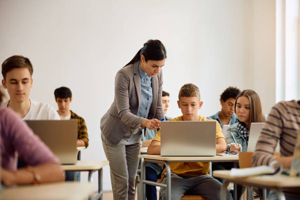 istock Female teacher assisting high school student during computer class in the classroom. 1576356470