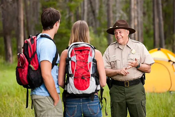 A friendly park ranger stops to talk to two backpackers near their tent in the woods. Nice and friendly conversation.