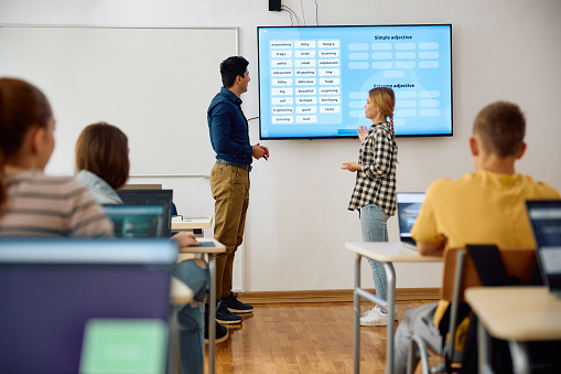 High school teacher and female student using interactive whiteboard on a class in the classroom.