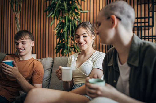 Three people, man and two women having coffee while sitting on sofa at home.