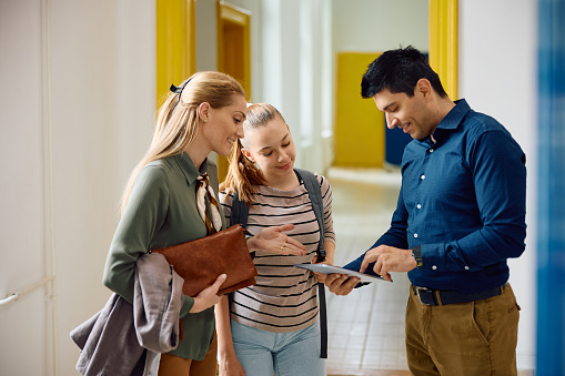 High school principal using digital tablet during a meeting with female student and her mother in hallway.