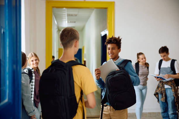 istock Happy black student taking laptop out of his backpack while talking to a classmate at high school hallway. 1576360458
