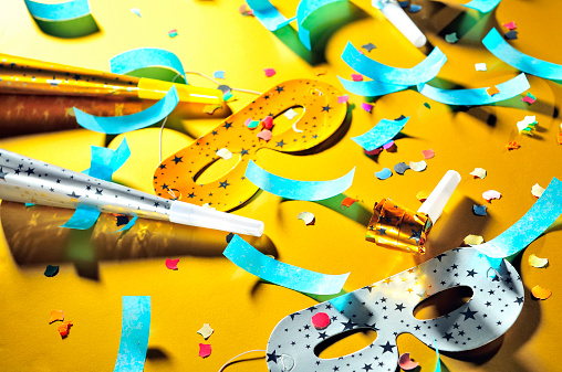 Let's celebrate! Mess after party, decorations: masks, whistles, horns, confetti are scattered on the floor, golden background.