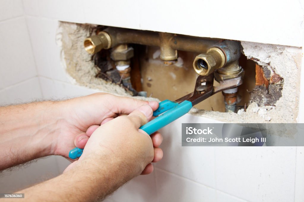 Shower Leak Plumber's hands have a two fisted grip on a wrench as he loosens a nut to fix a leak in a shower Plumber Stock Photo