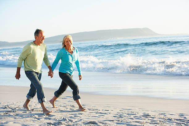 casal sênior caminhando ao longo da praia - retirement couple beach senior adult - fotografias e filmes do acervo