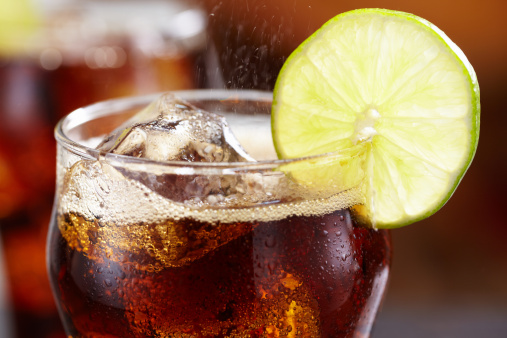 Tight shot of glass of cola with lime slice, shot with shallow focus on top of drink.  Fizz shooting out of top of drink