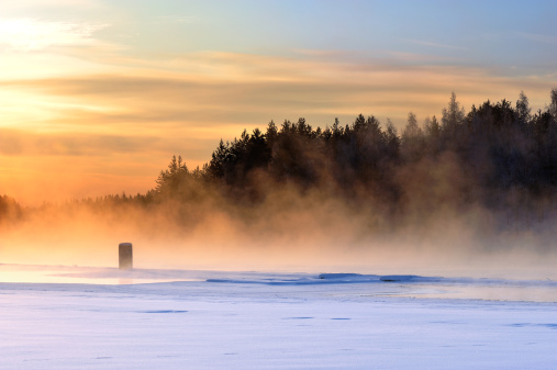 Mist over freezing river on a cold winter. Sunset view.