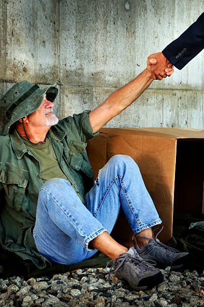 Government Official Giving Grateful Veteran a Hand Up A Vietnam war veteran (actual) appears to be down and out. In this shot he is getting a hand up (not a hand out) from a suited arm, symbolic of government assistance. Scene staged. mike cherim stock pictures, royalty-free photos & images