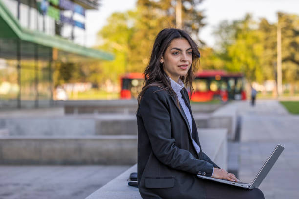 istock Serious business woman working hard and solving business problem on her laptop. She is sitting outdoors near modern office center. 1576379128