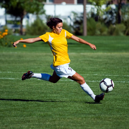 Female football player running to kick ball during match on pitch.