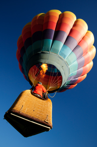 A brightly colored hot air balloon launching with its burner wide open