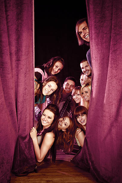 Young actors on stage Group of young adult actors looking from behind a purple curtain on theatre stage. They laughing and having fun. stage actress stock pictures, royalty-free photos & images
