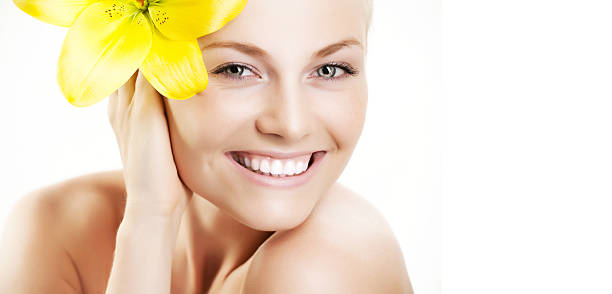 Serene portrait of a young woman in natural beauty holding a white lily flower. The photograph highlights a minimalist aesthetic with soft lighting, creating an atmosphere of purity, tranquility, and elegance. Perfect for themes of skincare, wellness, natural beauty, and florals.