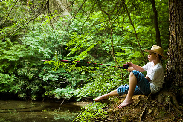 young boy fishing in a pond while leaning on a  big tree - with a retro vintage look